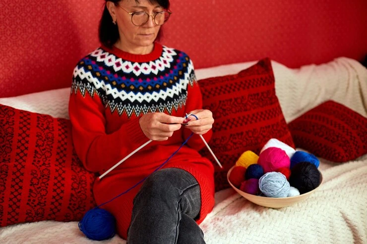 kvinne sitter komfortabelt i sofaen og strikker mens eldre kvinne strikker